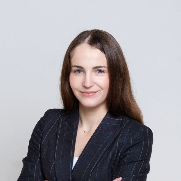 Headshot of Joanie Brunner, a white female with long brown hair, wearing a dark, pin-striped suit and crossing her arms while looking into the camera and smiling.