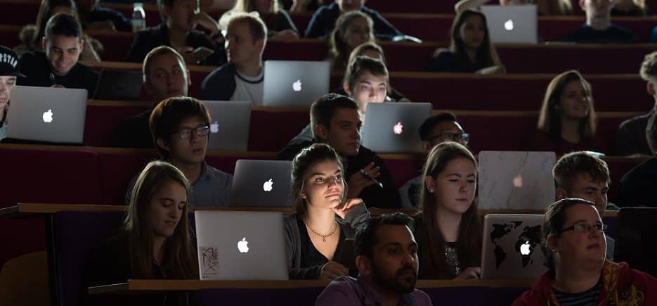 The image shows a lecture hall full of students. They are all studying on their laptops.