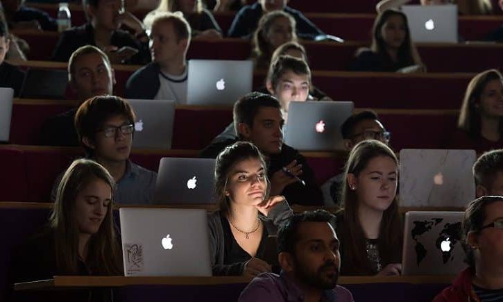 The image shows a lecture hall full of students. They are all studying on their laptops.